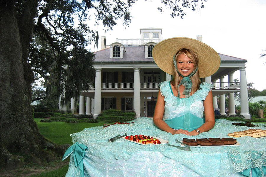 A woman in a hat standing in front of a table.