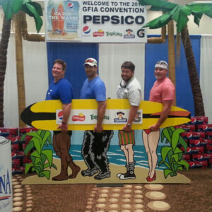 Three men posing in front of a Beach Legs Cutout sign.