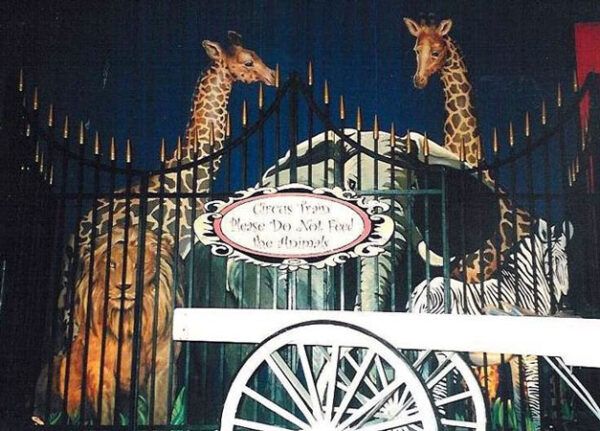 A giraffe and a zebra in front of Circus Animal Flats gate.