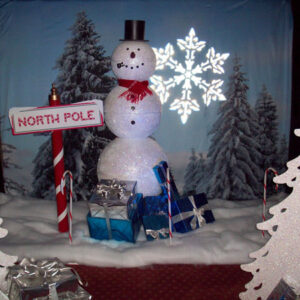 A North Pole Snowman in front of a Christmas tree.