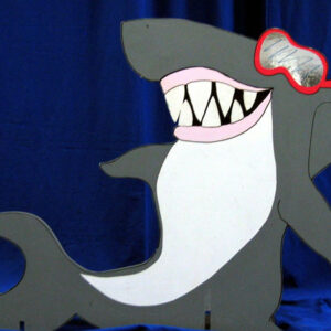 A Shark Cutouts with sunglasses and goggles is standing on a blue background.