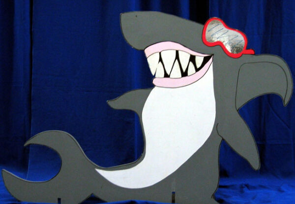 A Shark Cutouts with sunglasses and goggles is standing on a blue background.