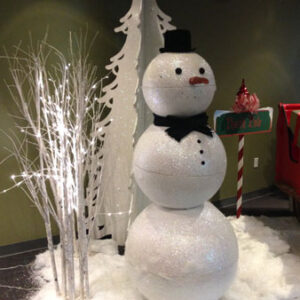 A North Pole Snowman is standing in front of a Christmas tree.