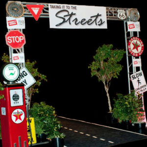 An archway with Street Signs and a gas station.