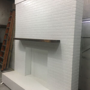 A white brick fireplace with a wooden shelf.