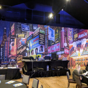 A large room with tables and chairs in front of a Times Square Backdrop.