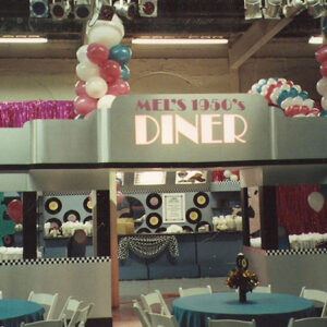 A table set up with balloons and a Custom Diner with Decor sign that says Mexican diner.