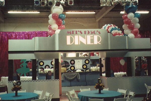 A table set up with balloons and a Custom Diner with Decor sign that says Mexican diner.