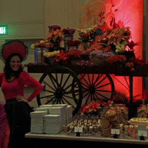 A woman dressed in a mexican costume standing next to a Flower Cart and Theme Actor.