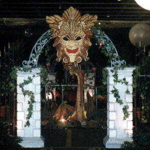 A Fire Eater dressed in a mask is standing in front of a gate.