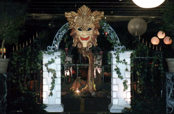 A Fire Eater dressed in a mask is standing in front of a gate.