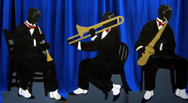 Three black men sitting on chairs with Character Flats trumpets and saxophones.