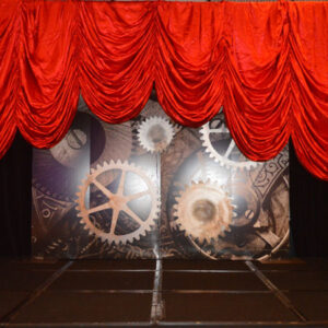 A stage set with a red curtain and a clock.