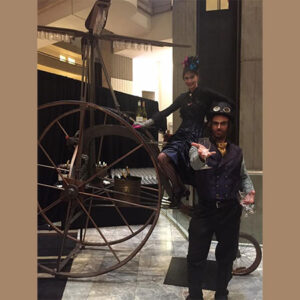 Steampunk Characters standing next to a steam powered bicycle.