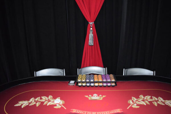 A Texas Hold'em table with a red curtain and chairs.