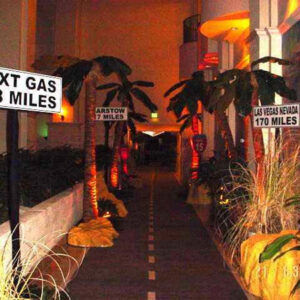 A Vegas Roadway with palm trees and a sign that says next gas 156 miles.