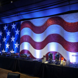 An Illuminated Flag backdrop in a room with tables and chairs.