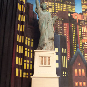 The Statue of Liberty is on stage in front of a city.