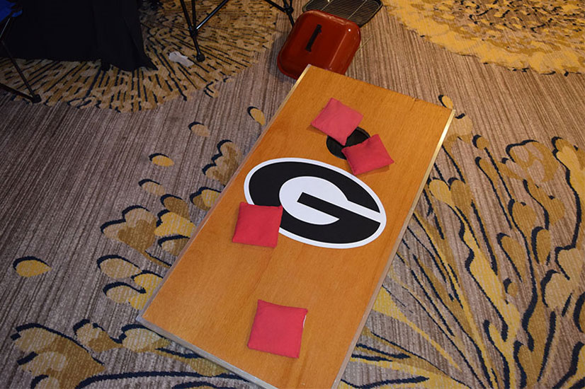 An outdoor team game of cornhole on a carpet.