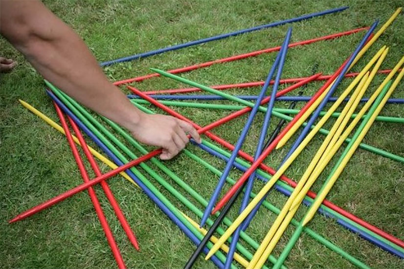 A person enjoying a game of yard games with a bunch of colored sticks on the grass.