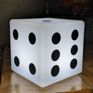 A white Glow Dice with black dots on it sits on a table.